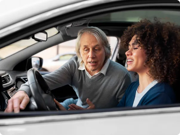 Homme âgé et femme plus jeune discutant dans une voiture neuve.