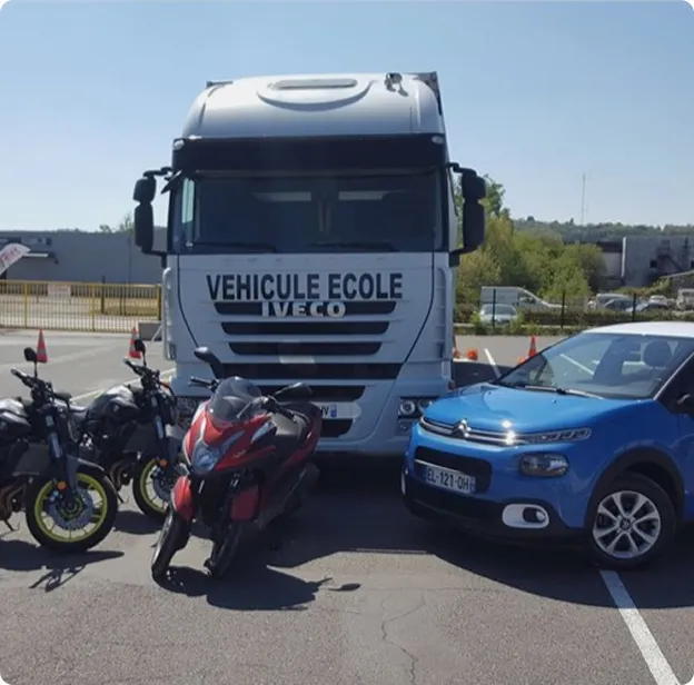 Camion auto-école Iveco, voitures bleues et motos garées à l'extérieur.