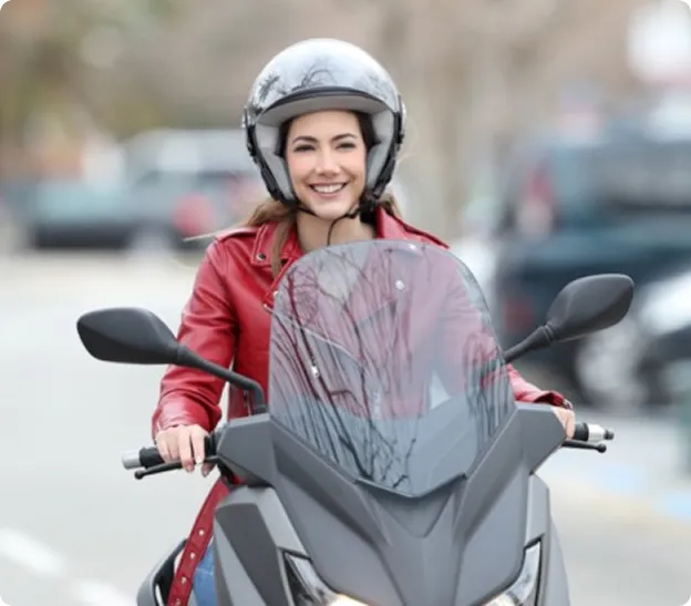 Jeune femme souriante, casquée, sur un scooter gris avec un blouson rouge.