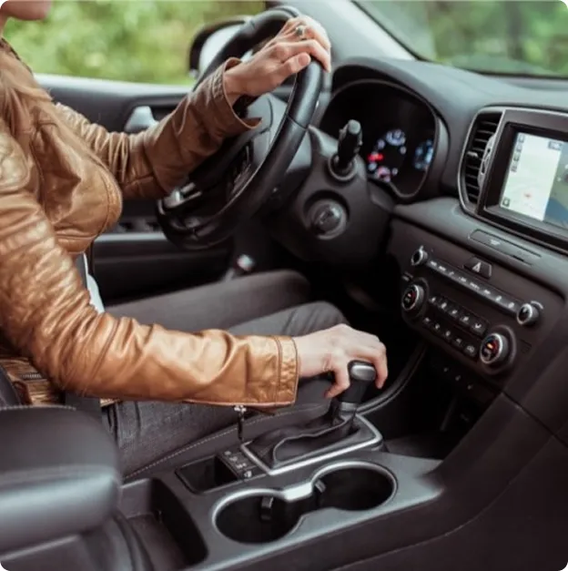 Femme en veste de cuir marron conduisant, main sur le volant et levier de vitesses.