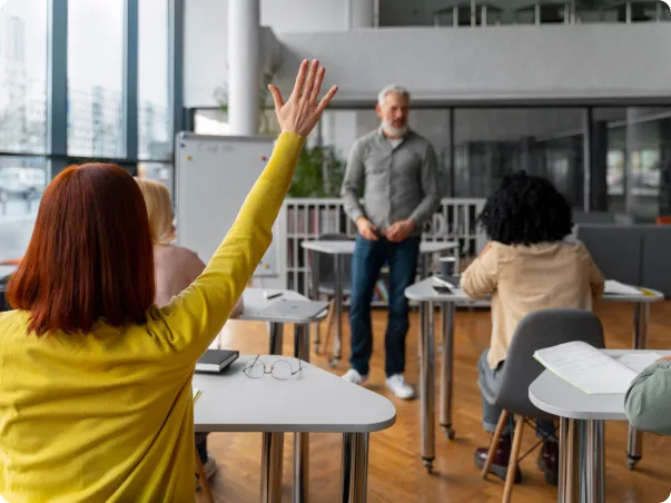 Étudiant levant la main en classe, avec un professeur et d'autres étudiants.