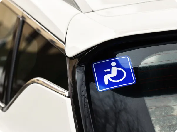 Autocollant bleu et blanc pour fauteuil roulant sur la vitre arrière d'une voiture blanche.