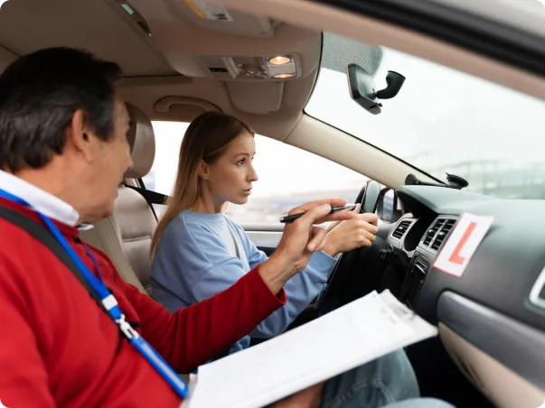 Un instructeur de conduite en rouge enseigne à une jeune femme blonde dans une voiture.