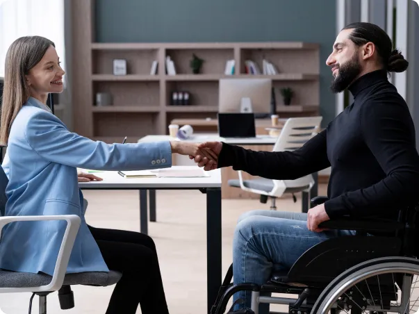 Une femme et un homme en fauteuil roulant se serrent la main dans un bureau.