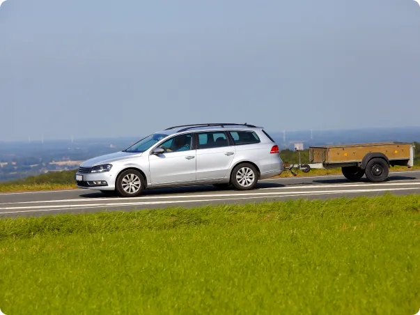 Une voiture familiale argentée tire une petite remorque sur une route bordée d'herbe.