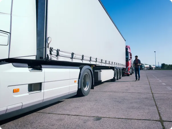 Un camionneur inspecte un poids lourd blanc sur un parking ensoleillé.