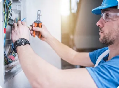 Électricien en casque et lunettes de sécurité travaillant sur un tableau électrique.