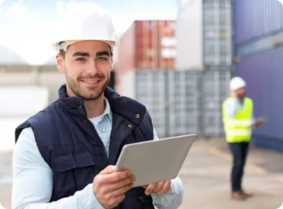 Homme souriant en gilet et casque de sécurité, tenant une tablette dans un port conteneurs.