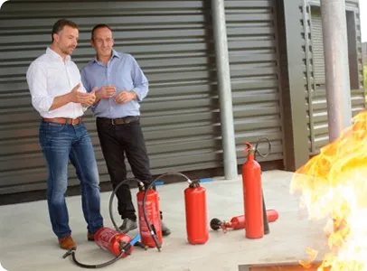 Deux hommes devant des extincteurs et un feu lors d'une formation.