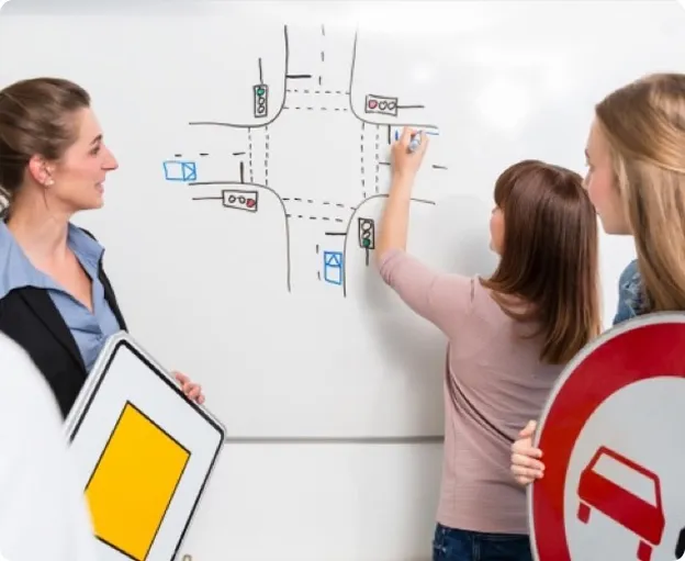 Trois femmes apprennent le code de la route avec un tableau blanc et des panneaux.